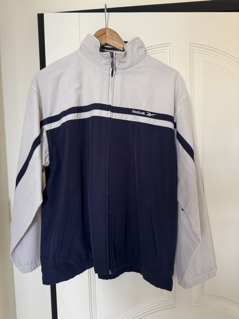 Reebok Track and Field Jacket (Category: Coats, Jackets and Outerwear) located in Singapore. Submitted by paperhandsss (Listing ID 1441405349, Image 1). Description: - Classic Reebok track jacket - Navy and white colorway - Stripes on sleeves - Full zip front - Stand-up collar - Two front pockets - Ideal for casual wear or sports.
