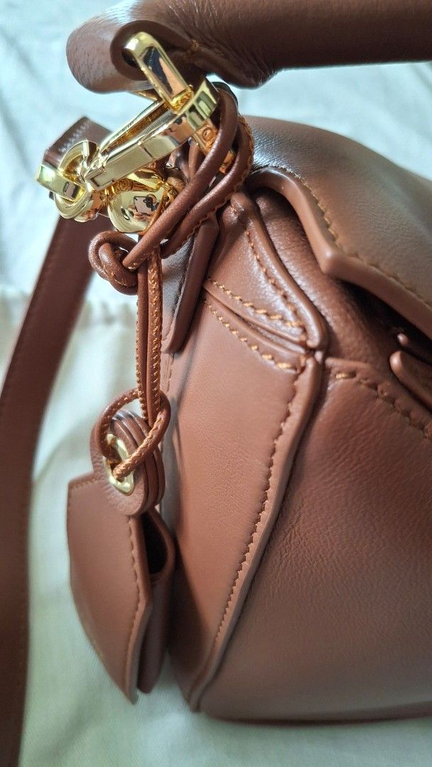 Loewe Puzzle Bag Featherlight with dustbag (Category: Luxury Bags & Wallets) located in Angono. Submitted by bagamania (Listing ID 1444961964, Image 3). Description: - Genuine brown leather Loewe bag - Secure zipper closure - Detachable strap for versatile wear - Interior with branded Loewe tag - Comes with a matching leather luggage tag - Elegant gold hardware details - Distinctive geometric design.