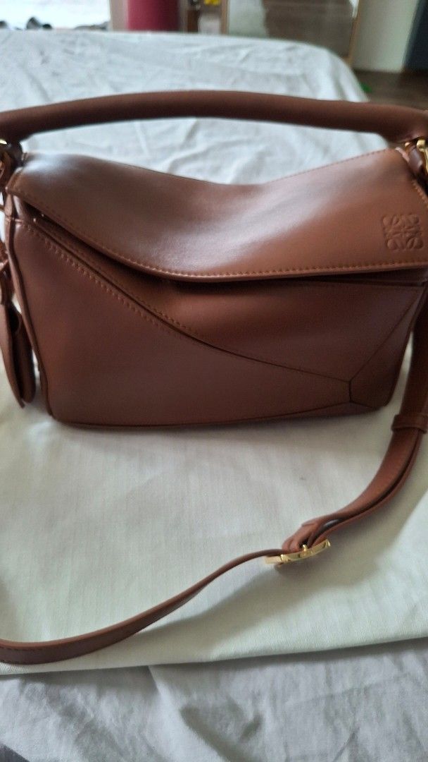 Loewe Puzzle Bag Featherlight with dustbag (Category: Luxury Bags & Wallets) located in Angono. Submitted by bagamania (Listing ID 1444961964, Image 1). Description: - Genuine brown leather Loewe bag - Secure zipper closure - Detachable strap for versatile wear - Interior with branded Loewe tag - Comes with a matching leather luggage tag - Elegant gold hardware details - Distinctive geometric design.