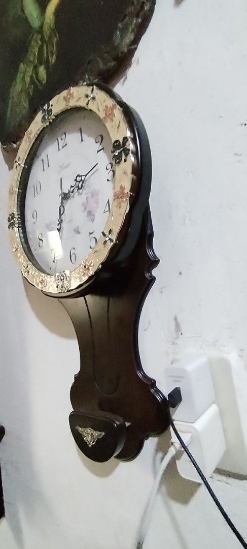 Vintage Style Pendulum Wall Clock with Floral Design (Category: Clocks) located in Caloocan City. Submitted by rowely_jpn (Listing ID 1444991461, Image 3). Description: Decorative wall clock with a pendulum. Features a classic round face with Arabic numerals. The bezel has a floral and butterfly motif. The dark wood casing has an ornate pendulum. Adds a vintage charm to any room. Works well working ,battery operated ..