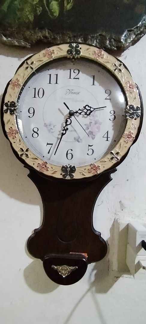Vintage Style Pendulum Wall Clock with Floral Design (Category: Clocks) located in Caloocan City. Submitted by rowely_jpn (Listing ID 1444991461, Image 2). Description: Decorative wall clock with a pendulum. Features a classic round face with Arabic numerals. The bezel has a floral and butterfly motif. The dark wood casing has an ornate pendulum. Adds a vintage charm to any room. Works well working ,battery operated ..