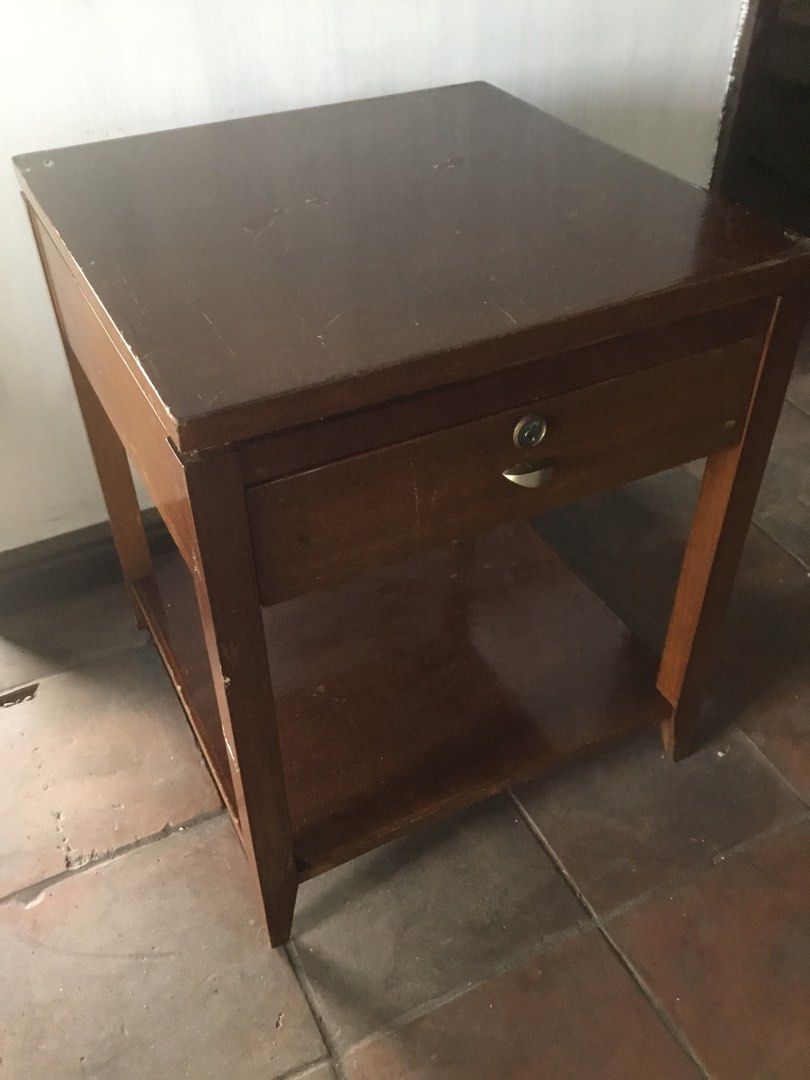 Wooden Side Table with Drawer and Shelf (Category: Tables & Sets) located in Manila. Submitted by roberto.enriquez (Listing ID 1444918400, Image 1). Description: - Brown wooden side table - Features one drawer with a lock and key - Includes an additional shelf for storage - Shows minor scratches and wear from use, indicating character - Sturdy and reliable construction - Ideal as a bedside table or end table Height 24 Table top 20 X 20 inches .