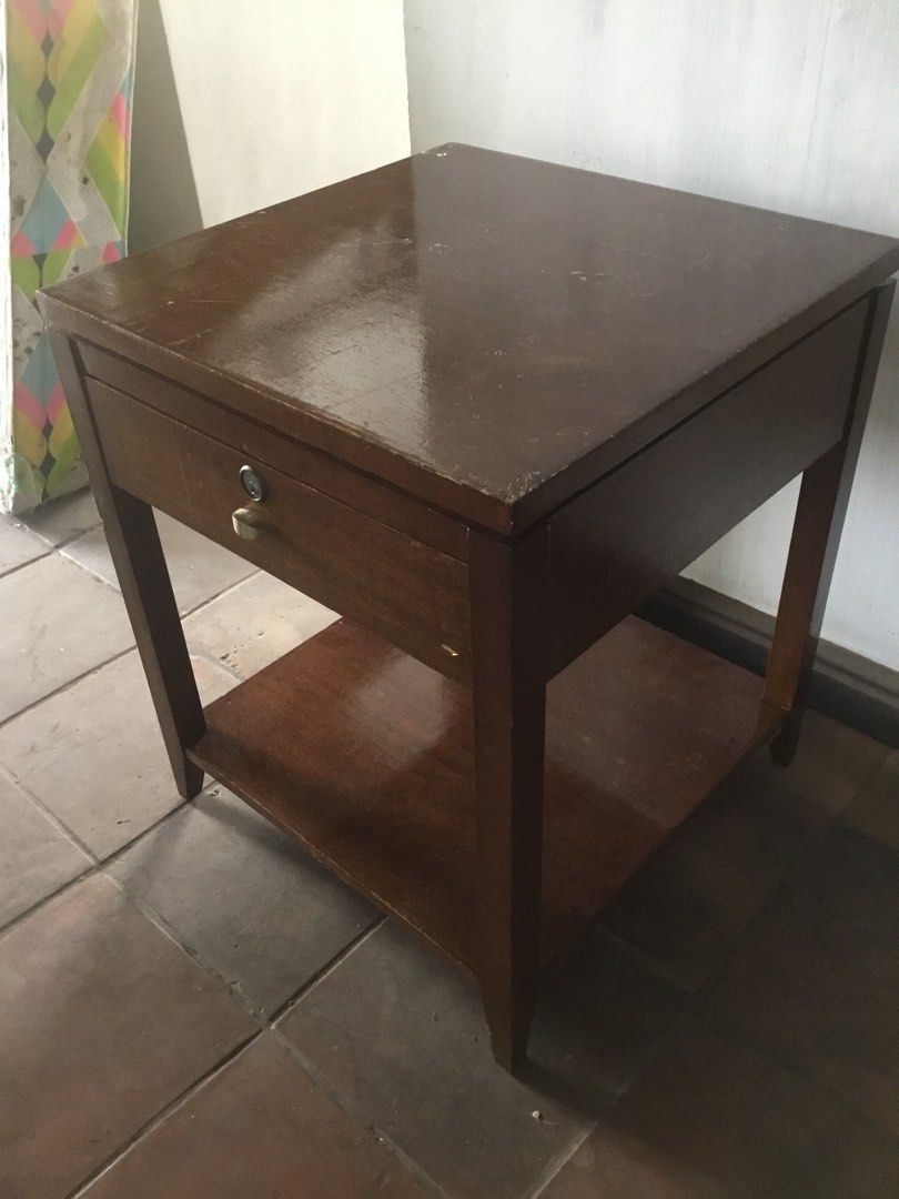Wooden Side Table with Drawer and Shelf (Category: Tables & Sets) located in Manila. Submitted by roberto.enriquez (Listing ID 1444918400, Image 3). Description: - Brown wooden side table - Features one drawer with a lock and key - Includes an additional shelf for storage - Shows minor scratches and wear from use, indicating character - Sturdy and reliable construction - Ideal as a bedside table or end table Height 24 Table top 20 X 20 inches .