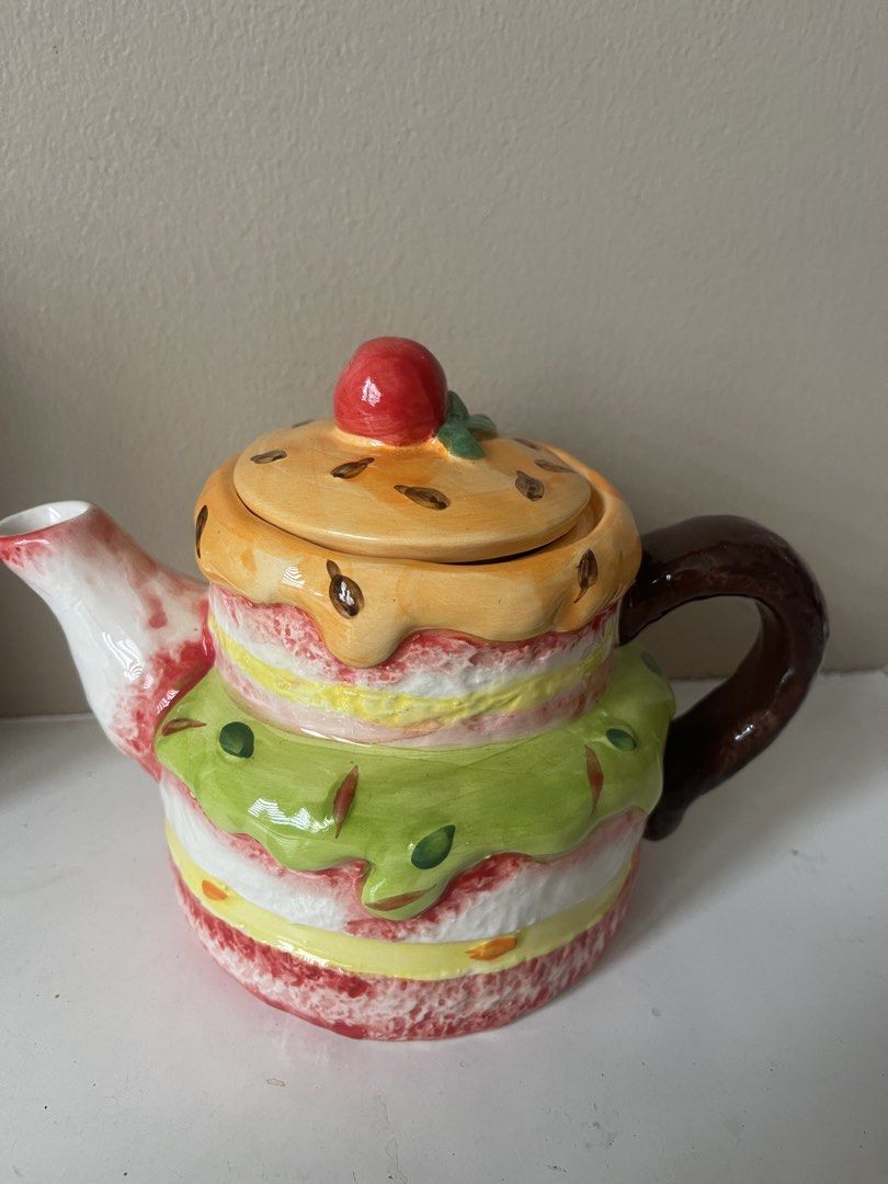 Cute Cake Shaped Ceramic Teapot (Category: Coffee & Tea Tableware) located in San Juan City. Submitted by miggyenriquez (Listing ID 1445071173, Image 2). Description: - Adorable teapot shaped like a tiered cake - Features colorful frosting details and a cherry on top - Lid lifts off to reveal the opening - Ideal for tea parties or as a quirky kitchen decoration - Well-defined handle and spout - A fun piece for any collection.
