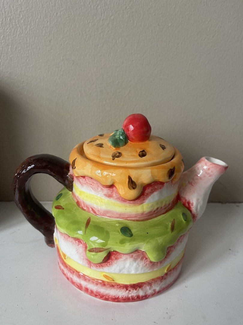 Cute Cake Shaped Ceramic Teapot (Category: Coffee & Tea Tableware) located in San Juan City. Submitted by miggyenriquez (Listing ID 1445071173, Image 1). Description: - Adorable teapot shaped like a tiered cake - Features colorful frosting details and a cherry on top - Lid lifts off to reveal the opening - Ideal for tea parties or as a quirky kitchen decoration - Well-defined handle and spout - A fun piece for any collection.