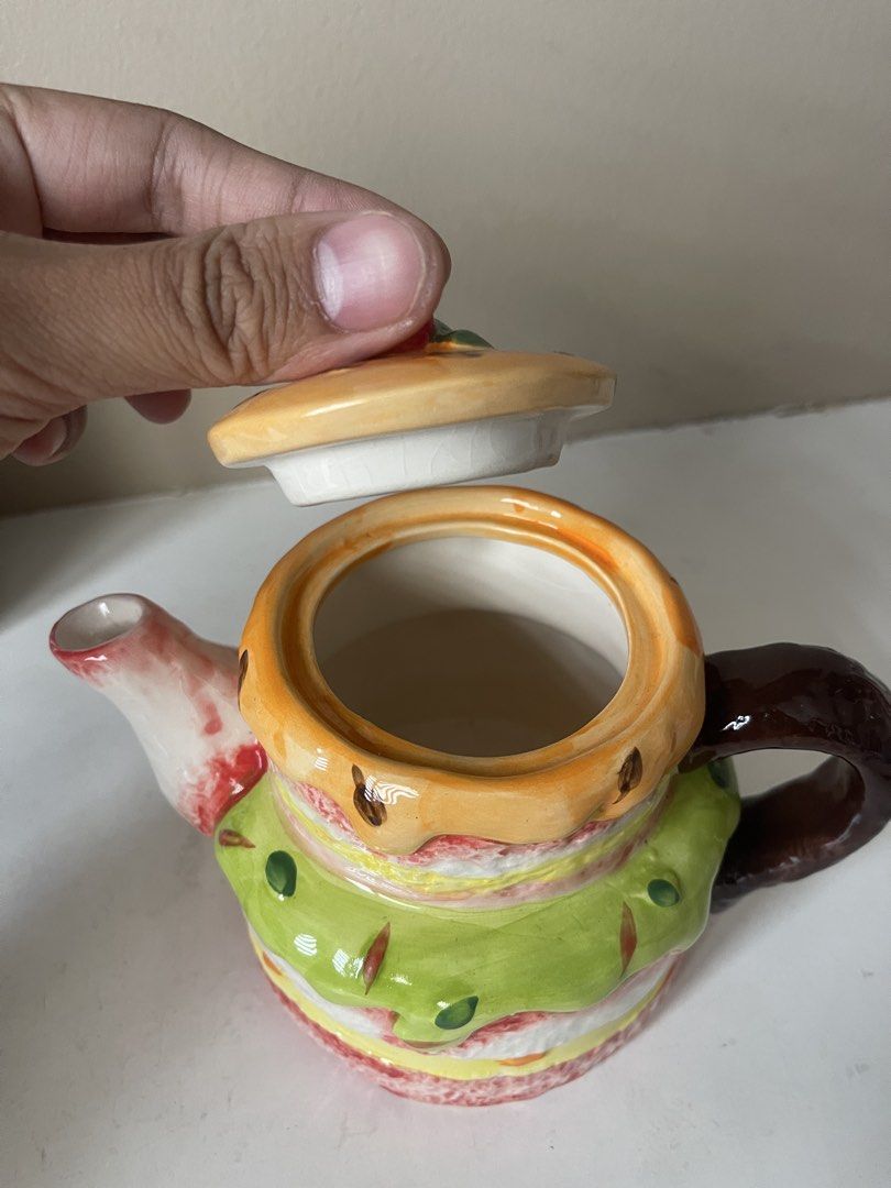 Cute Cake Shaped Ceramic Teapot (Category: Coffee & Tea Tableware) located in San Juan City. Submitted by miggyenriquez (Listing ID 1445071173, Image 3). Description: - Adorable teapot shaped like a tiered cake - Features colorful frosting details and a cherry on top - Lid lifts off to reveal the opening - Ideal for tea parties or as a quirky kitchen decoration - Well-defined handle and spout - A fun piece for any collection.