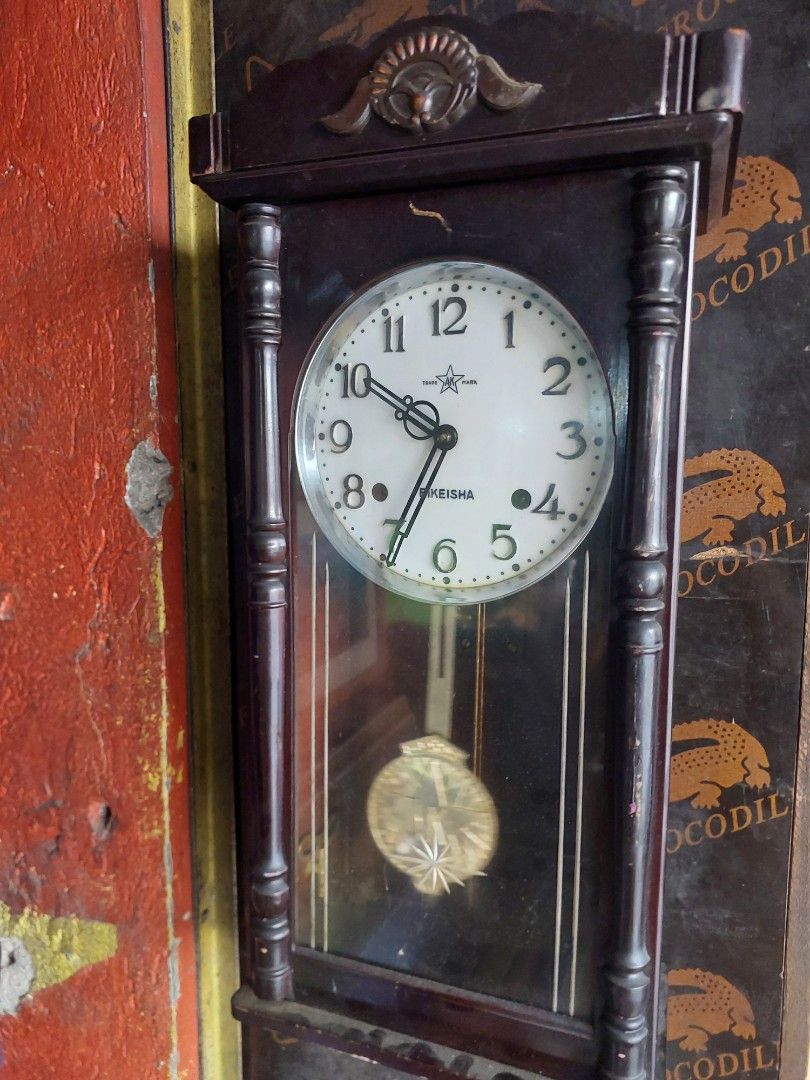 Keisha Wooden Mantel Clock with Pendulum (Category: Clocks) located in Quezon City. Submitted by jpnvintageonline (Listing ID 1445139704, Image 3). Description: - Vintage Keisha mantel clock - Dark wood casing with decorative carvings - White face with black Roman numerals - Features a swinging pendulum - Includes winding key - Perfect for display or as a functional timepiece - Adds a classic touch to any room.