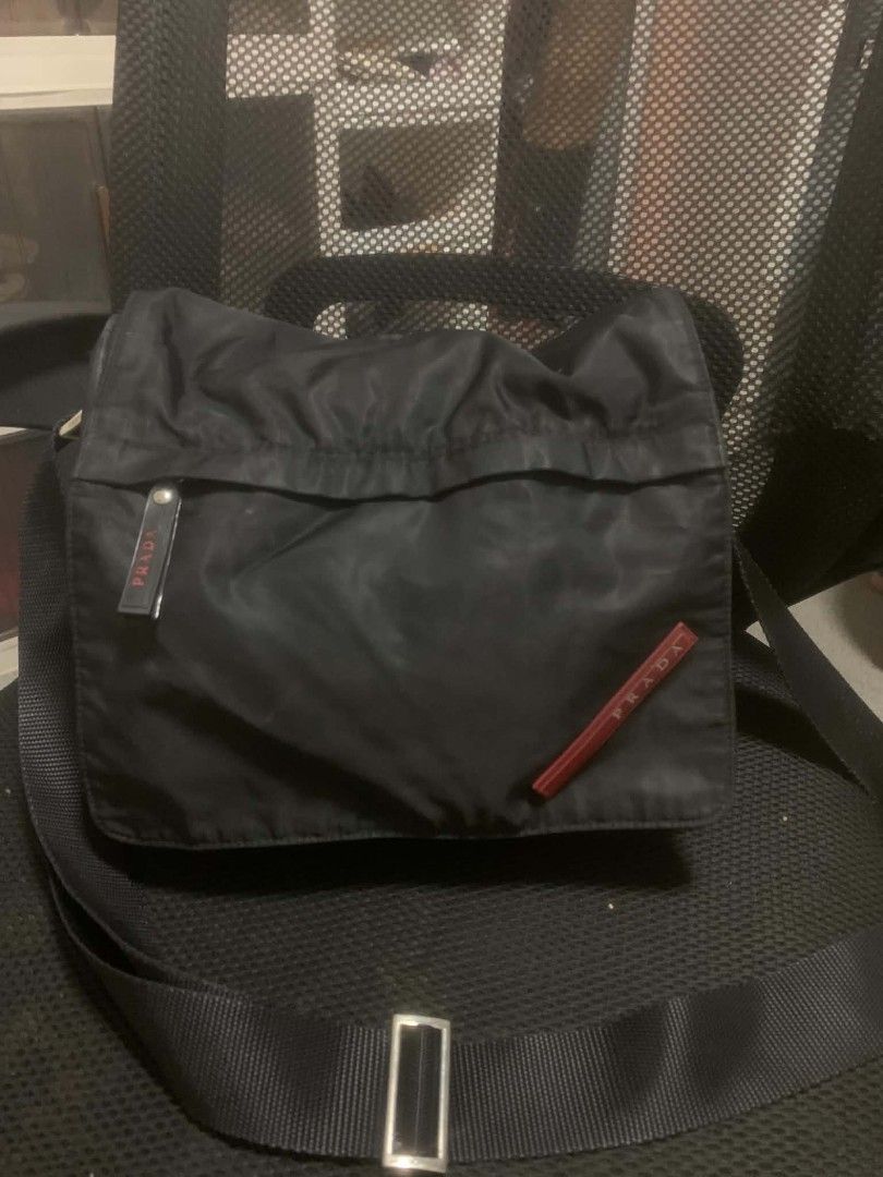 Prada Black Nylon Crossbody Bag (Category: Luxury Bags & Wallets) located in Quezon City. Submitted by ukaybag.ph09 (Listing ID 1445052674, Image 2). Description: - Prada crossbody bag - Durable nylon material - Front pocket with signature red Prada logo - Adjustable strap with metal buckle - Secure zipper closure - Minor marks on front (please check photos for details) - Ideal for everyday wear.