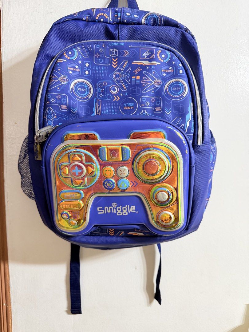 Smiggle Blue Gaming Controller Backpack (Category: Backpacks) located in Manila. Submitted by thedigital28748 (Listing ID 1445055170, Image 1). Description: - Cool blue Smiggle backpack - Fun gaming controller design on front pocket - Spacious interior for books and essentials - Comfortable padded shoulder straps - Convenient side mesh pocket for water bottle - Ideal for kids who love gaming.