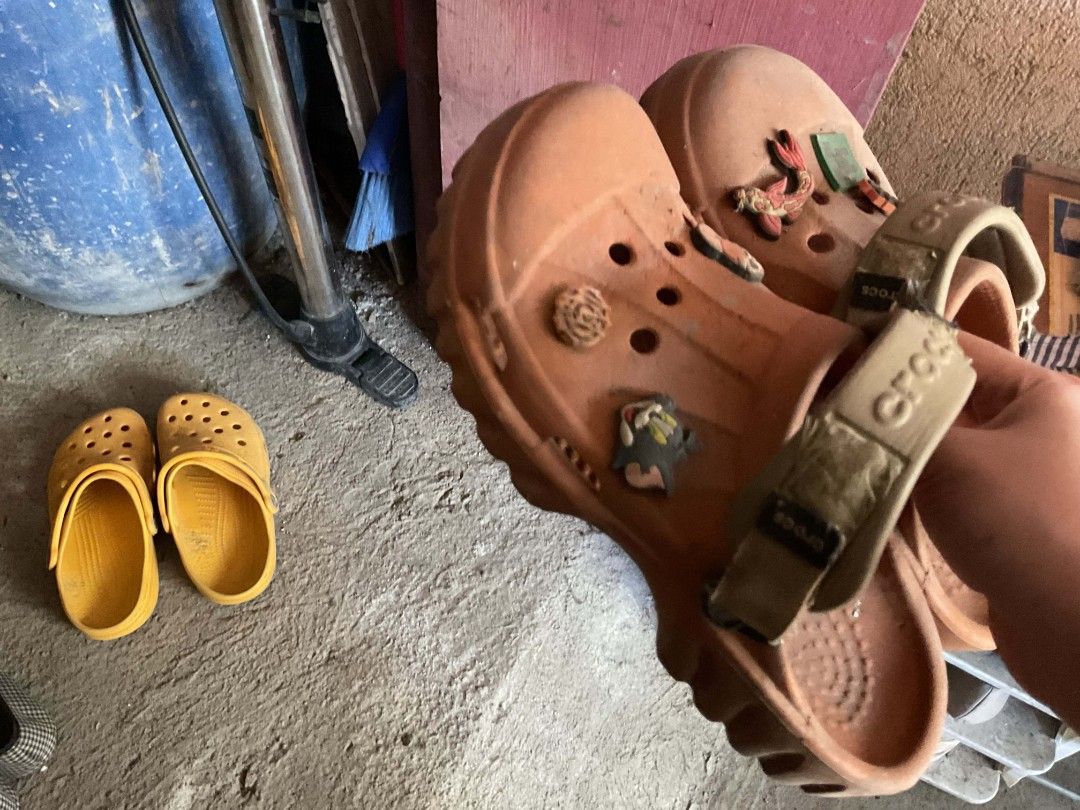 TAKE ALL Crocs Clogs with Jibbitz Charms (Category: Slippers and slides) located in Manila. Submitted by declutterthisandthat (Listing ID 1445061197, Image 1). Description: - Bundle includes two pairs of used Crocs clogs. - One pair is brown and features Jibbitz charms. - The brown pair's strap has the Crocs logo. - The second pair is yellow. - Both pairs are sold as a set. !!! need lang i wash ng water marumi lang sa pic!!!! isang classic orange