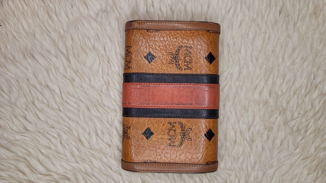 MCM Visetos Trifold Wallet Cognac (Category: Luxury Bags & Wallets) located in Cavite. Submitted by amairos (Listing ID 1445235058, Image 2). Description: - Authentic MCM trifold wallet - Classic Visetos monogram print - Signature cognac color with black and red stripe detail - Gold-tone hardware - Multiple card slots and compartments - Snap closure - Shows some signs of wear on leather and edges.