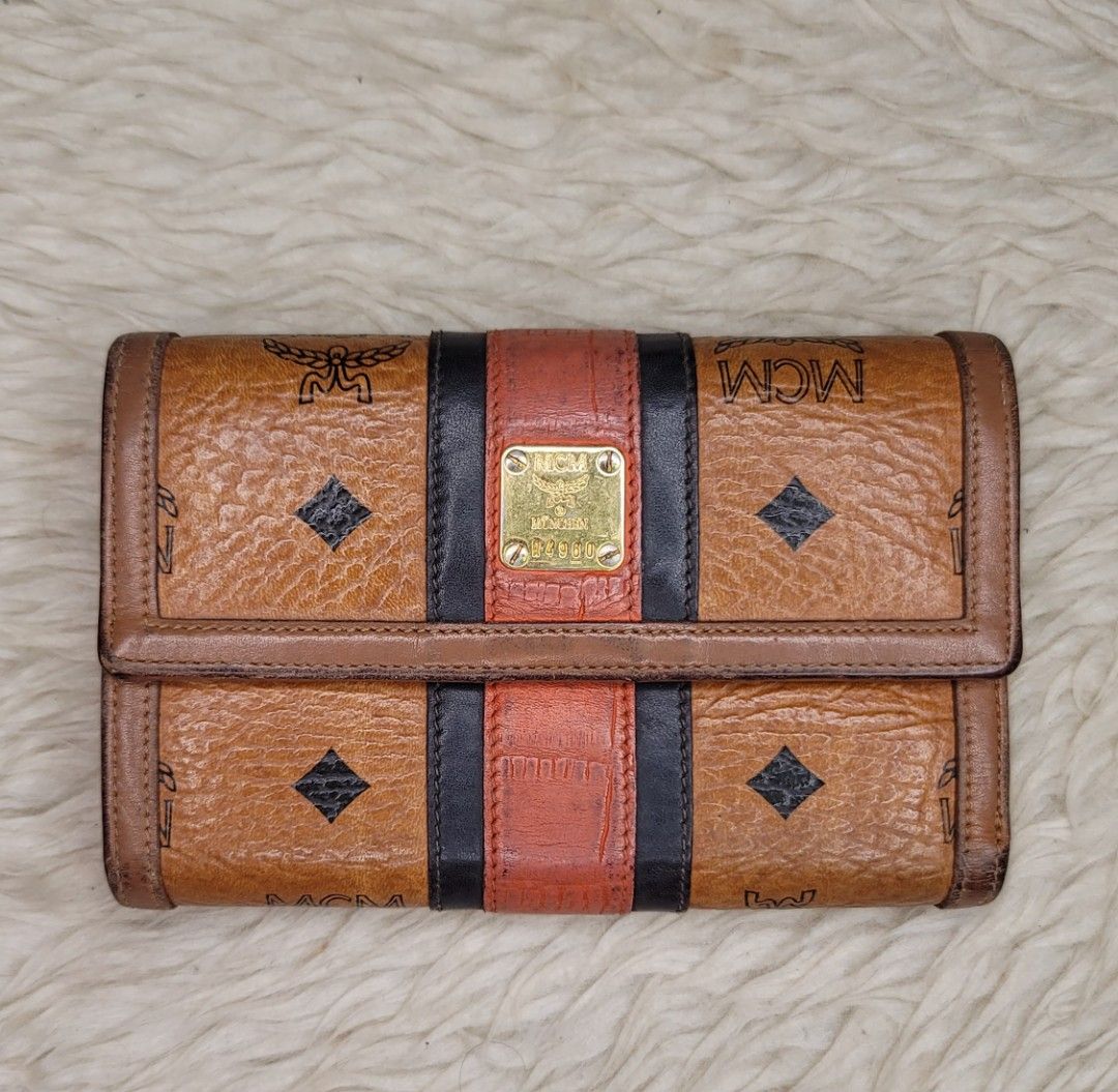 MCM Visetos Trifold Wallet Cognac (Category: Luxury Bags & Wallets) located in Cavite. Submitted by amairos (Listing ID 1445235058, Image 1). Description: - Authentic MCM trifold wallet - Classic Visetos monogram print - Signature cognac color with black and red stripe detail - Gold-tone hardware - Multiple card slots and compartments - Snap closure - Shows some signs of wear on leather and edges.