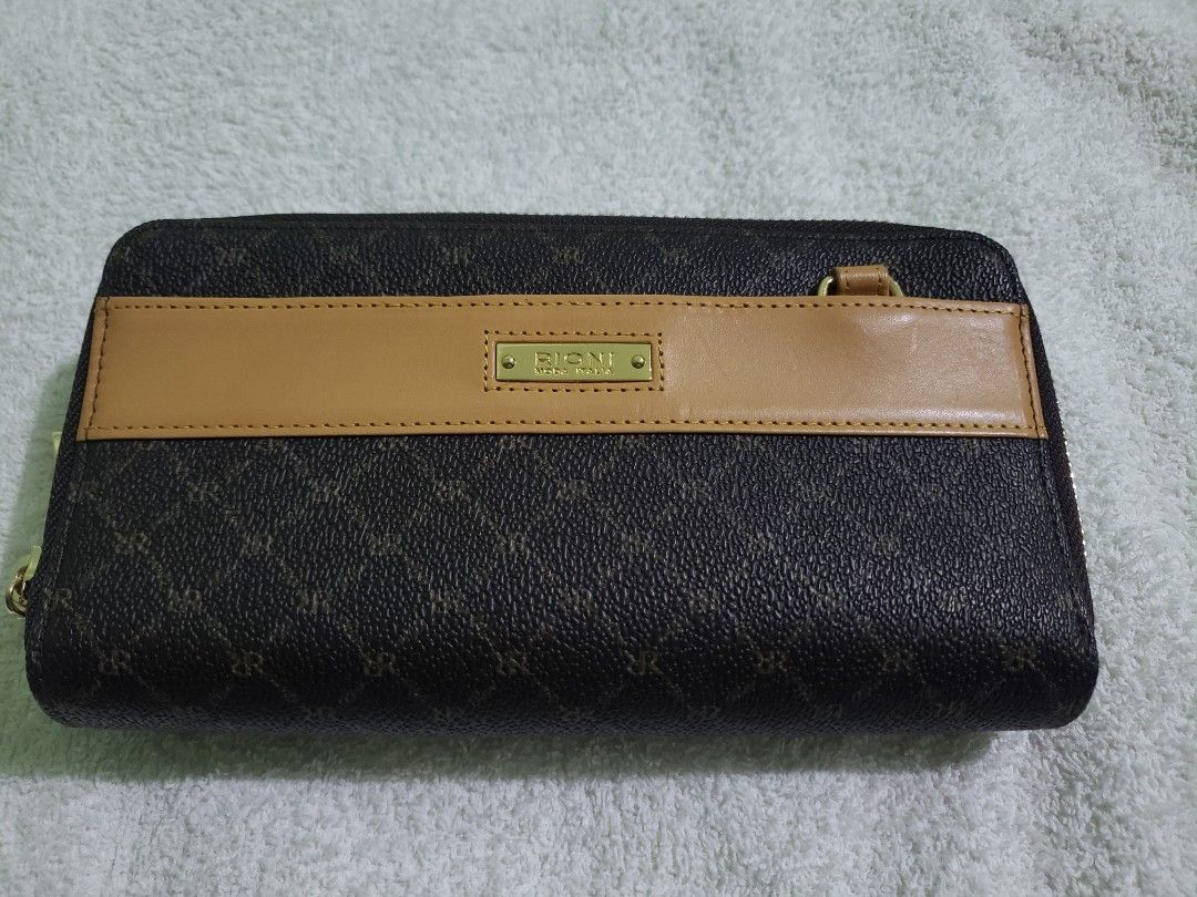 RIONI Leather Dual Zip Wallet with Strap (Category: Luxury Bags & Wallets) located in Navotas City. Submitted by miloklo (Listing ID 1445534700, Image 2). Description: - Authentic RIONI wallet with signature monogram print. - Tan leather accent band on the front. - Secure zipper closure. - Interior features multiple card slots and a clear ID window. - Comes with a detachable crossbody strap. - Almost new with original tags..