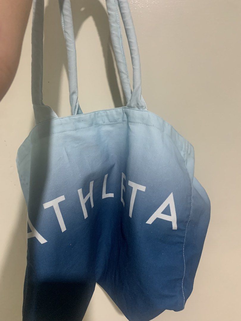 Athleta Ombre Blue White Canvas Tote Bag (Category: Tote Bags) located in Pasig City. Submitted by declutterapparel (Listing ID 1445727402, Image 2). Description: - Large Athleta tote bag - Stylish ombre design: white to deep blue - Clear Athleta logo on the front - Ideal for beach, gym, or everyday errands - Spacious interior for all your essentials - Comfortable carrying straps.