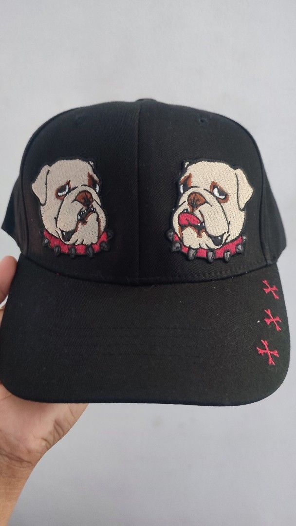 Black Baseball Cap with Bulldog Embroidery (Category: Caps & Hats) located in Manila. Submitted by janyvony_315 (Listing ID 1445753616, Image 3). Description: - Black baseball cap - Embroidered design: Two bulldog faces with pink spiked collars on the front - Embroidered red cross-like symbols on the side of the brim - White cross symbols on the back - Adjustable strap for a comfortable fit - Camouflage pattern on the underside of the brim.