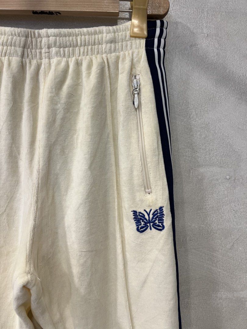 Needles Velour Narrow Track Pants (Category: Joggers) located in Manila. Submitted by -handpick- (Listing ID 1445750865, Image 2). Description: Cream velour track pants from Needles. Navy blue stripes down the sides. Embroidered butterfly logo on the left leg. Zipper pockets on both sides and one on the back. Elastic waistband with drawstring. Velour material feels soft. Great for casual wear. Size : Small on tag Dimensions : Length : 35.5 Inseam