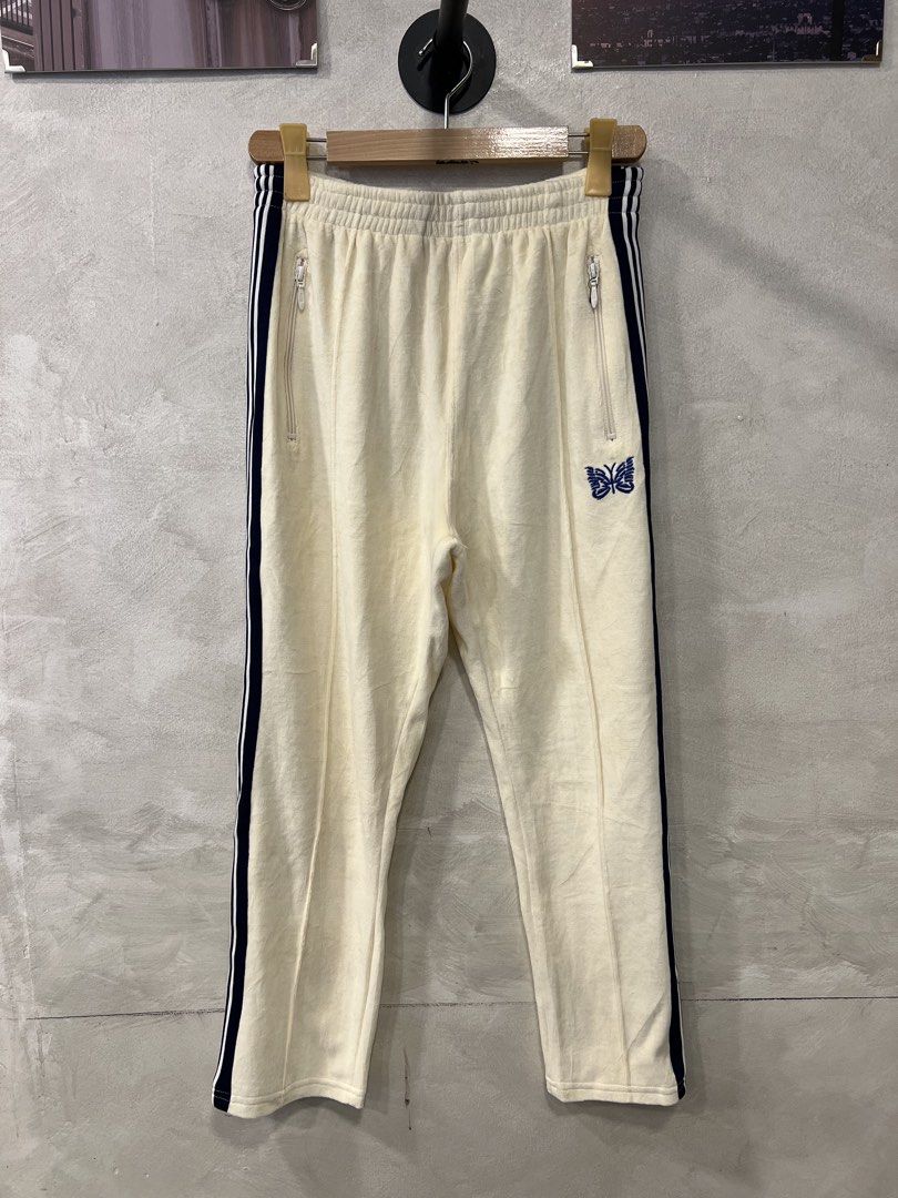 Needles Velour Narrow Track Pants (Category: Joggers) located in Manila. Submitted by -handpick- (Listing ID 1445750865, Image 1). Description: Cream velour track pants from Needles. Navy blue stripes down the sides. Embroidered butterfly logo on the left leg. Zipper pockets on both sides and one on the back. Elastic waistband with drawstring. Velour material feels soft. Great for casual wear. Size : Small on tag Dimensions : Length : 35.5 Inseam