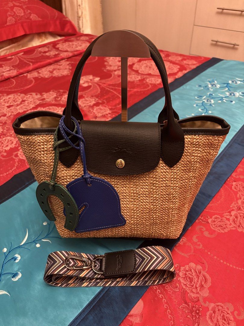 Longchamp Straw Tote Bag with Charms and Strap (Category: Luxury Bags & Wallets) located in Mandaue City. Submitted by jane2872 (Listing ID 1446071232, Image 1). Description: - Stylish straw tote bag - Accented with black leather trim and handles - Includes two adorable charms: a green horseshoe and a blue helmet - Features a vibrant, colorful patterned crossbody strap (authentic) - authentic longchamp strap - Ideal for summer adventures and outi