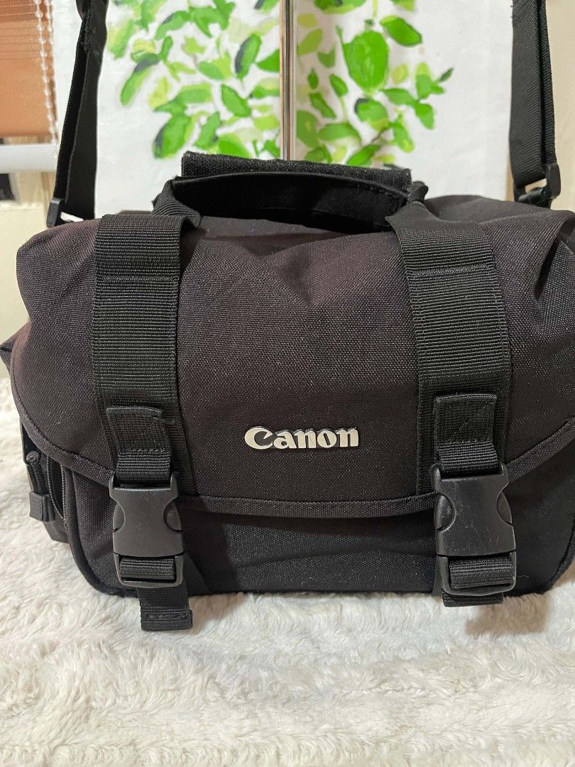 Canon Black Camera Bag with Adjustable Strap (Category: Camera Bags & Carriers) located in Naawan. Submitted by twilly.apparel2 (Listing ID 1446185863, Image 2). Description: - Genuine Canon camera bag - Durable material for protection - Spacious main compartment for camera - Convenient side pockets for accessories - Adjustable shoulder strap for comfortable carrying - Secure buckle closures on front flap.