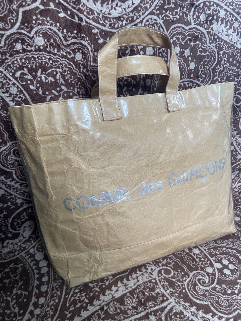 CDG COMME des GARÇONS PVC Tote Bag (Category: Luxury Bags & Wallets) located in Pili. Submitted by rgthriftflip29 (Listing ID 1446277266, Image 2). Description: - Authentic COMME des GARÇONS tote bag - Unique brown paper-like texture with a clear plastic overlay - Built with sturdy handles and a reinforced base for durability - Spacious interior, perfect for everyday essentials or shopping trips - Chic and minimalist design that complements any o