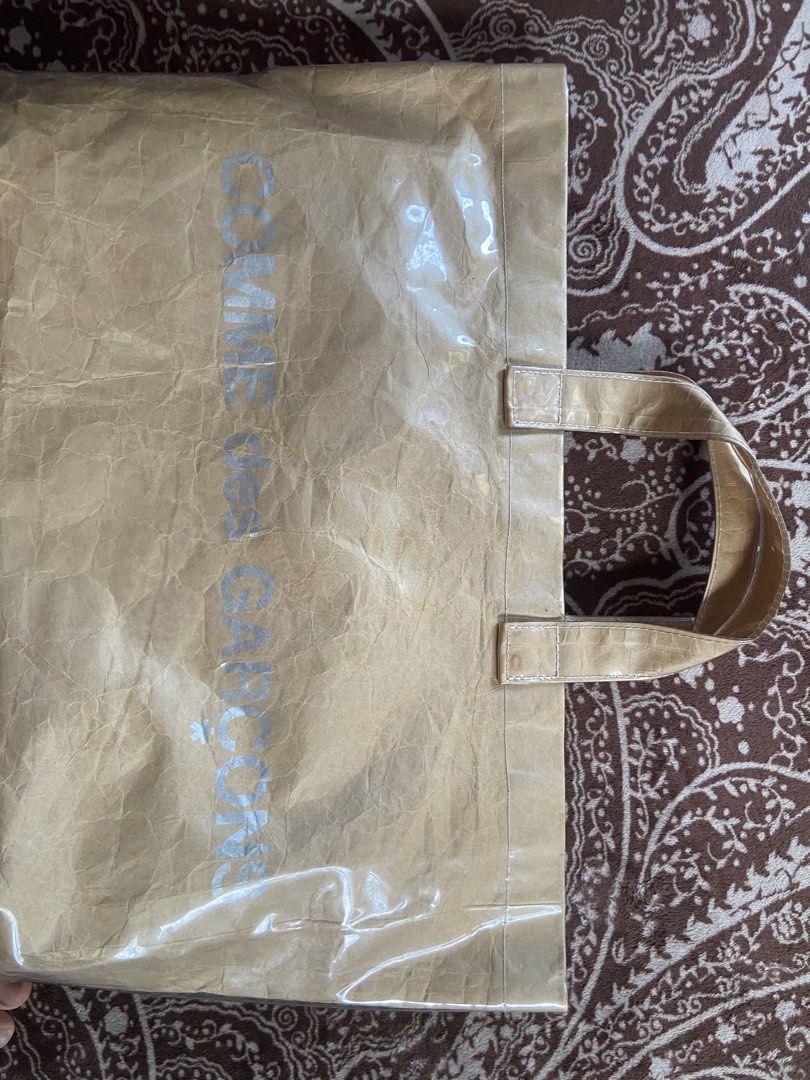 CDG COMME des GARÇONS PVC Tote Bag (Category: Luxury Bags & Wallets) located in Pili. Submitted by rgthriftflip29 (Listing ID 1446277266, Image 3). Description: - Authentic COMME des GARÇONS tote bag - Unique brown paper-like texture with a clear plastic overlay - Built with sturdy handles and a reinforced base for durability - Spacious interior, perfect for everyday essentials or shopping trips - Chic and minimalist design that complements any o