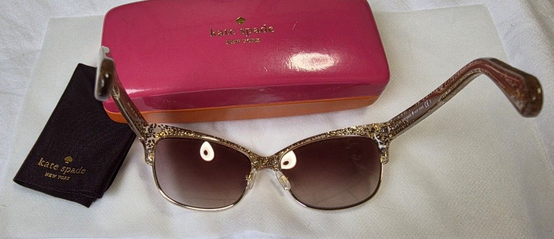 Kate Spade New York Sunglasses with Case (Category: Sunglasses & Eyewear) located in Dasmarinas. Submitted by carousel111222 (Listing ID 1446242623, Image 2). Description: - Authentic Kate Spade New York sunglasses - Chic gold glitter frames - Stylish brown gradient lenses - Comes with original pink hard case featuring a cute eye design inside - Includes black cleaning cloth - Ideal accessory for sunny weather.