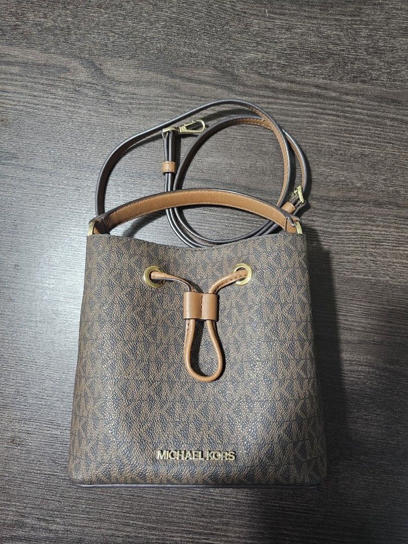 Michael Kors Monogram Bucket Bag (Category: Luxury Bags & Wallets) located in Cavite. Submitted by pink.kai.shop (Listing ID 1446326383, Image 2). Description: - Classic Michael Kors bucket bag - Brown monogram print with leather trim - Secure drawstring closure - Top handle and detachable shoulder strap - Elegant gold hardware details - Ideal for everyday wear With Flaws #sale #bag #michaelkors.