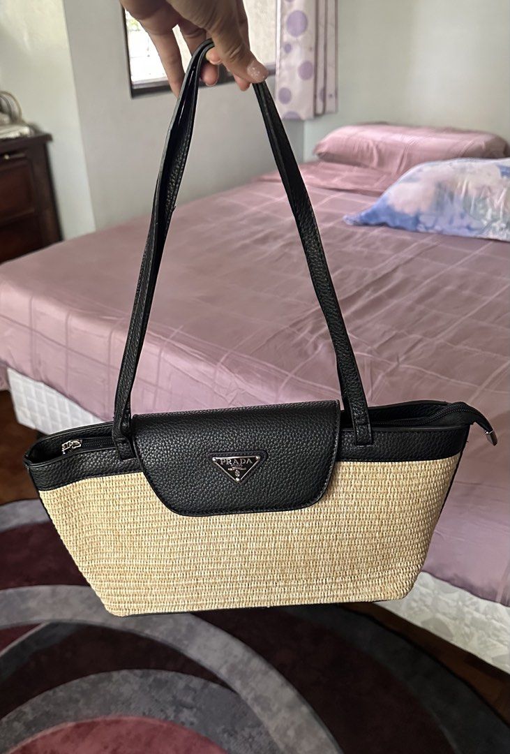 This Prada raffia and black leather tote bag (Category: Luxury Bags & Wallets) located in Makati City. Submitted by janeabat (Listing ID 1446220620, Image 2). Description: - Original GWP Prada - Woven straw body with black leather trim and handles - Iconic Prada triangle logo on front flap - Secure zipper closure at the top - Ideal for everyday use or beach days.