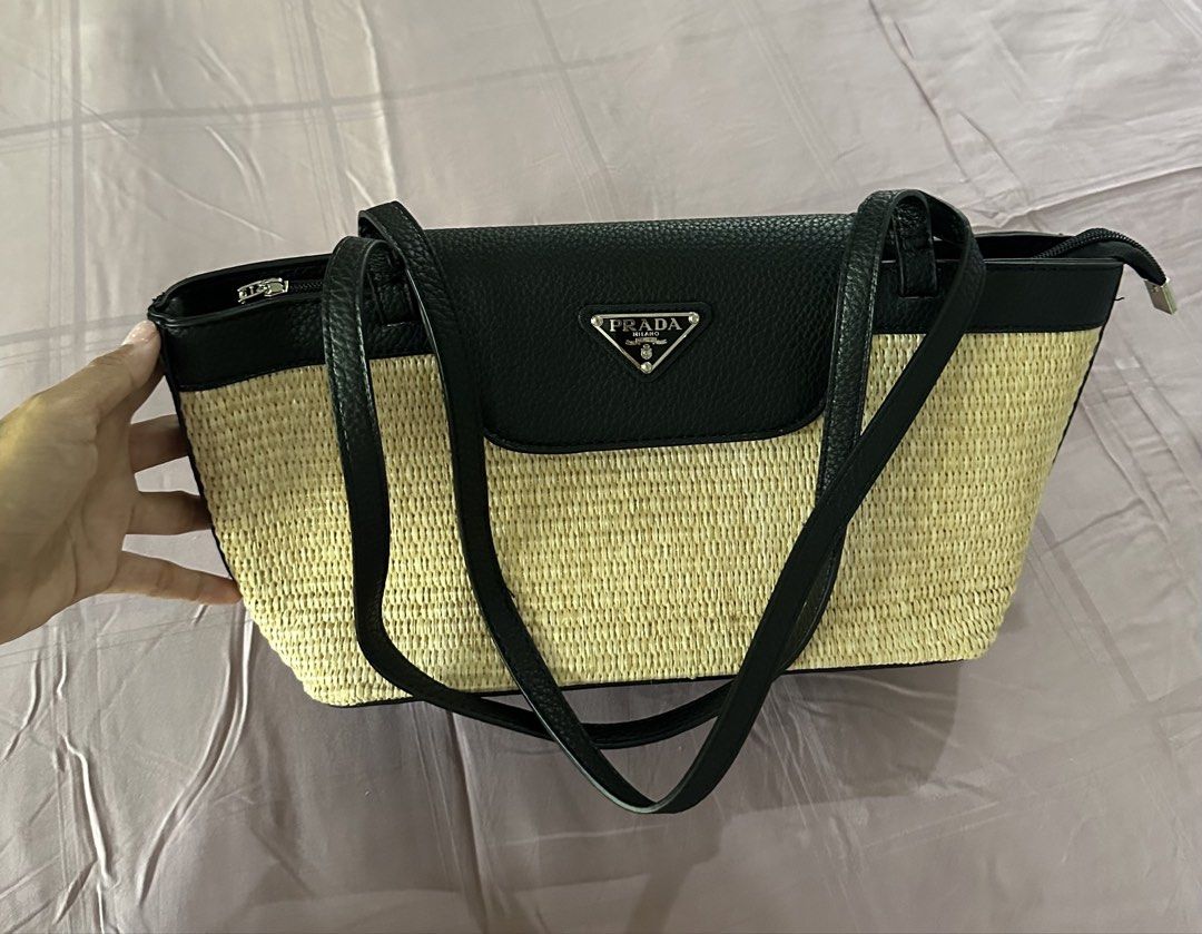 This Prada raffia and black leather tote bag (Category: Luxury Bags & Wallets) located in Makati City. Submitted by janeabat (Listing ID 1446220620, Image 1). Description: - Original GWP Prada - Woven straw body with black leather trim and handles - Iconic Prada triangle logo on front flap - Secure zipper closure at the top - Ideal for everyday use or beach days.