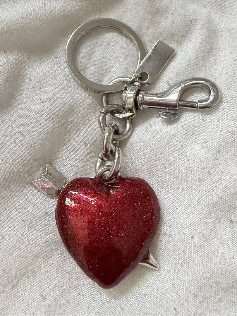 Coach Red Glitter Heart Arrow Keychain Charm (Category: Charms) located in Noveleta. Submitted by xtindc (Listing ID 1446355569, Image 2). Description: - Adorable Coach keychain - Features a red glitter heart with an arrow - Iconic 'C' logo detail - Durable silver hardware - Ideal for personalizing bags or keys - Adds a vibrant pop of color.