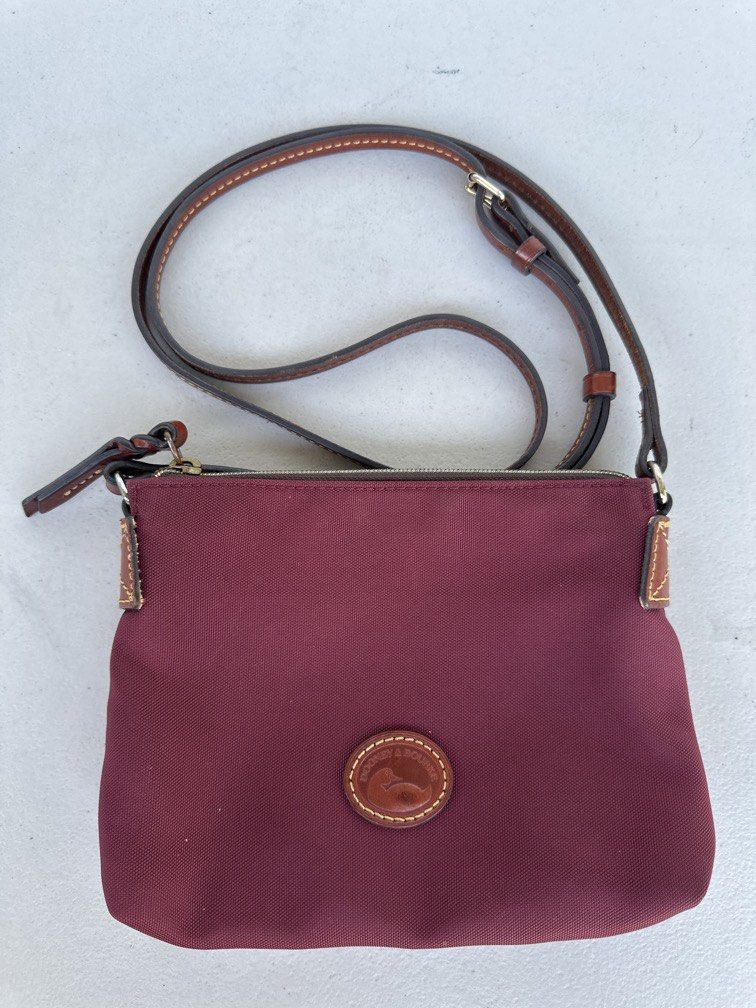 Dooney & Bourke Nylon Crossbody Pouchette (Category: Cross-body Bags) located in Manila. Submitted by classywardrobemanila (Listing ID 1446432571, Image 1). Description: Like new, just needs cleaning but all intact. Dooney & Bourke Nylon Crossbody Pouchette features a maroon nylon body and a stitched leather duck logo patch. Brand: Dooney & Bourke Material: Lightweight nylon with leather trim Features: Adjustable shoulder strap and a zip-top clos