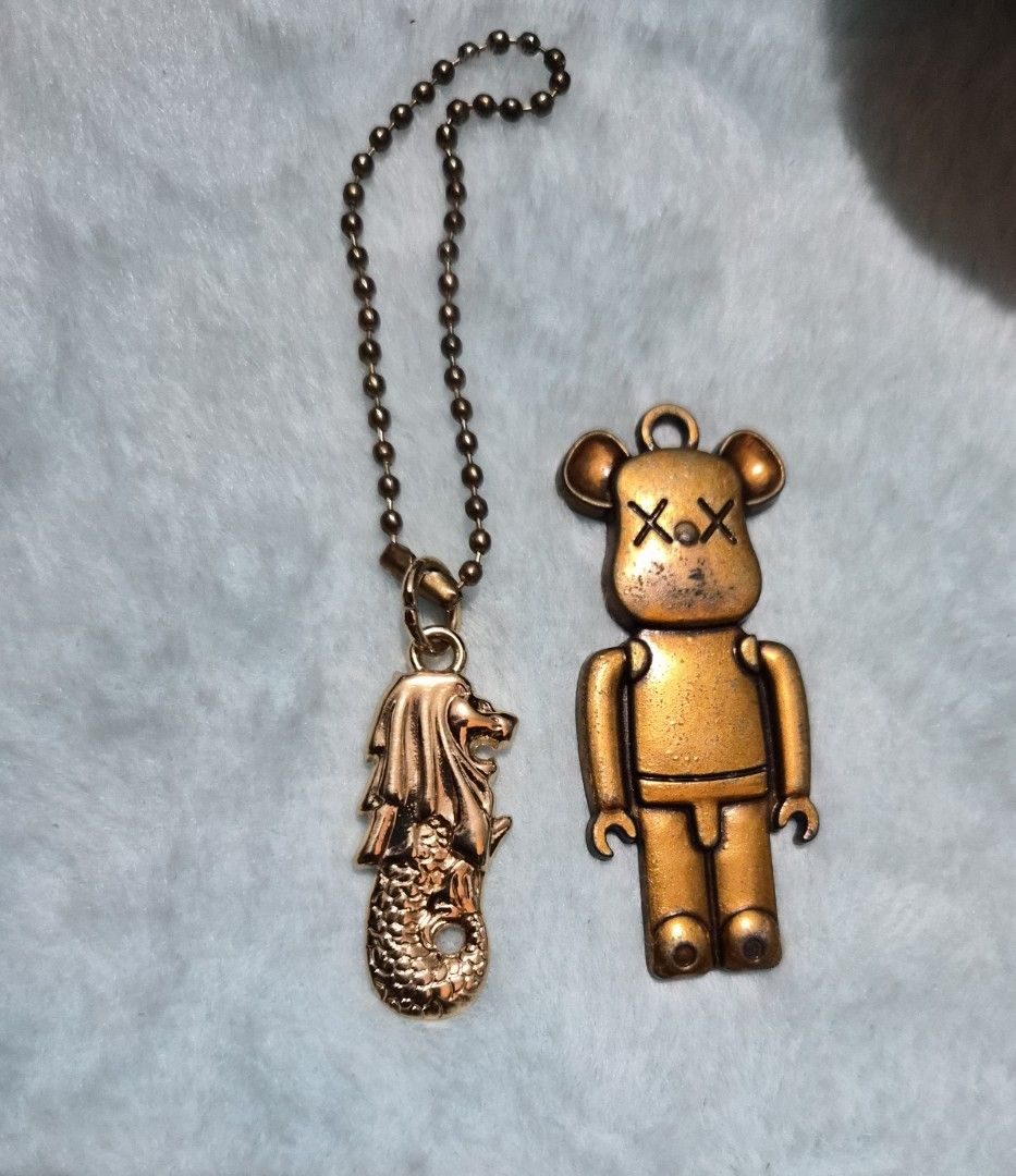 Merlion & Bearbrick Keychain Charms (Category: Character Goods) located in Mandaue City. Submitted by chuchi152615 (Listing ID 1446516962, Image 1). Description: - Set of 2 unique keychain charms - Vintage gold-tone finish - Features a Singapore Merlion icon - Includes a Bearbrick-style charm with X eyes - Ideal for decorating bags or keys - Great collectible pieces.