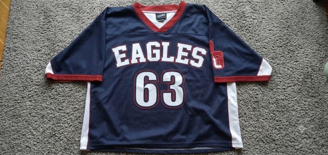 Erina Eagles Football Jersey (Category: Activewear) located in Manila. Submitted by 83ae4877f61519befe652aa8f5bf57 (Listing ID 1446614887, Image 1). Description: - Navy blue jersey with bold white 'EAGLES' text and '63' on the front. - Features striking red trim around the collar and sleeves. - Includes classic white side panels for a sporty look. - Small red '1' graphic accent on the right sleeve. - Ideal for any dedicated Eagles fan or for a co