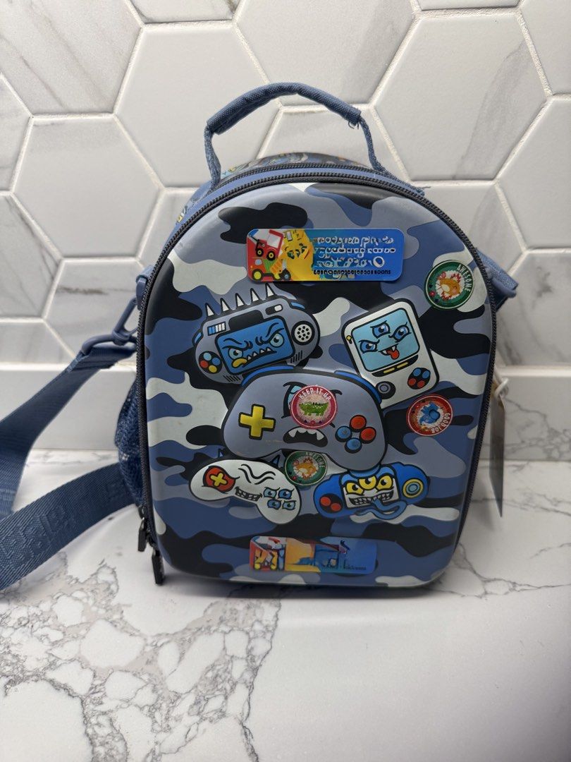 Smiggle Lunch Bag (Category: Babies & Kids Fashion) located in Cainta. Submitted by declutterwithme_476 (Listing ID 1446572937, Image 1). Description: - Smiggle lunch bag with cool blue camouflage and gaming controller design. - Main compartment for food and snacks. - Convenient side mesh pocket for drinks. - Adjustable shoulder strap for comfortable carrying. Stickers can be easily removed - Smiggle branded zippers for a stylish touch. - Ideal f