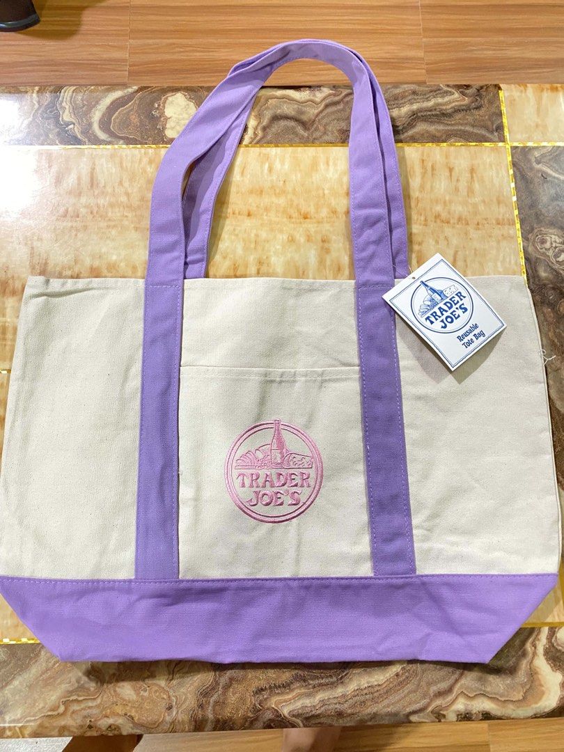 Trader Joe's Reusable Graphic Tote Bag (Category: Tote Bags) located in San Antonio. Submitted by pixiechromzzz (Listing ID 1446685003, Image 1). Description: - Trader Joe's Canvas Tote Bag from CALIFORNIA, USA - Color: Cream with purple accents - Features embroidered Trader Joe's logo on front - Includes a convenient front pocket - Material: 60% Cotton, 20% Polyester - Ideal for grocery shopping or everyday errands - Made in Vietnam.