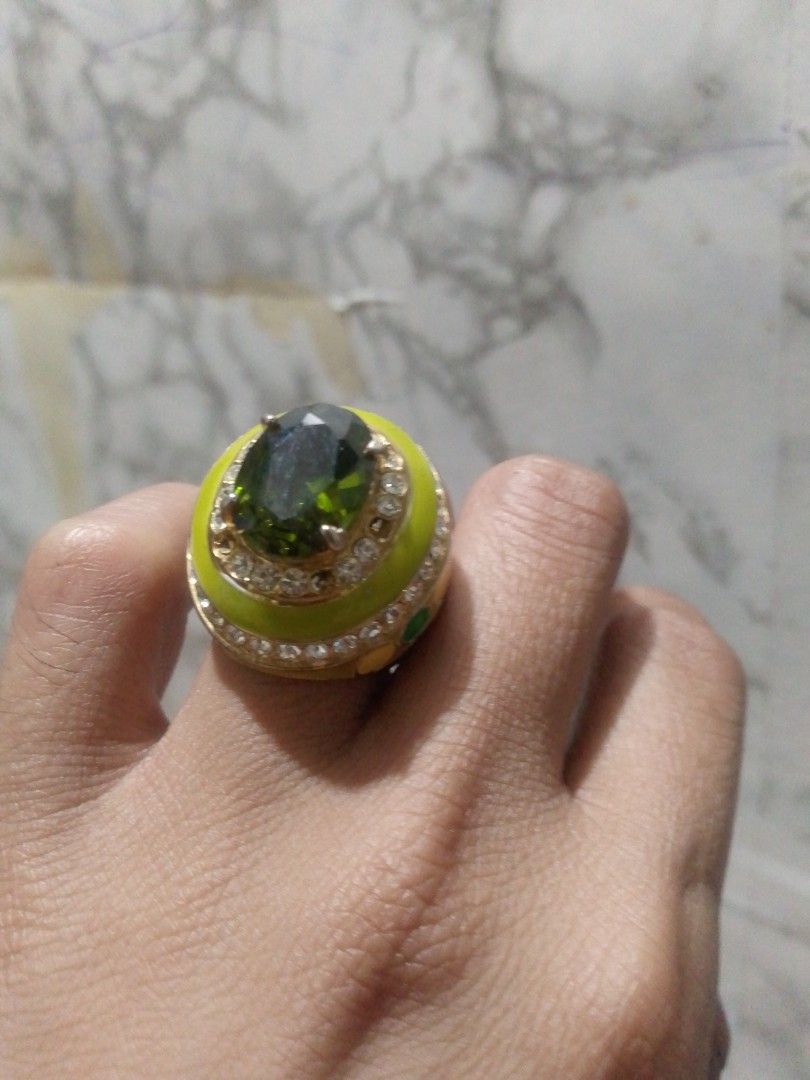 Gold Tone Ring with Green Stone and Crystals (Category: Rings) located in Manila. Submitted by epicwind_1bf746 (Listing ID 1441764095, Image 1). Description: - Eye-catching statement ring - Large green center stone - Surrounded by sparkling clear crystals - Gold-toned band with unique yellow enamel detail - Shows some signs of wear on the band.