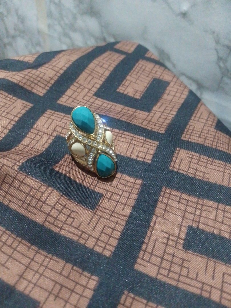 Gold Tone Statement Ring with Turquoise and White Stones (Category: Rings) located in Manila. Submitted by epicwind_1bf746 (Listing ID 1441764002, Image 3). Description: - Bold statement ring - Gold-tone metal base - Features two large teardrop turquoise stones - Accented with smaller white stones - Unique criss-cross band pattern - Perfect for adding a pop of color to any outfit.