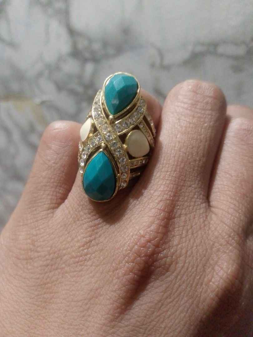 Gold Tone Statement Ring with Turquoise and White Stones (Category: Rings) located in Manila. Submitted by epicwind_1bf746 (Listing ID 1441764002, Image 2). Description: - Bold statement ring - Gold-tone metal base - Features two large teardrop turquoise stones - Accented with smaller white stones - Unique criss-cross band pattern - Perfect for adding a pop of color to any outfit.