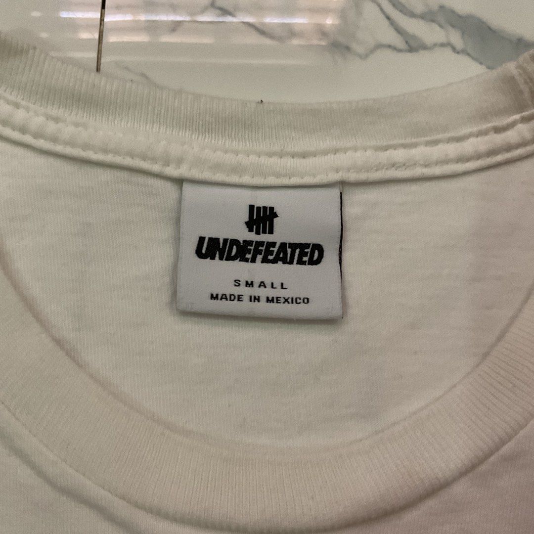 Undefeated White T-Shirt Size Small (Category: Tshirts & Polo Shirts ) located in Manila. Submitted by okeanos (Listing ID 1441773955, Image 3). Description: - Authentic Undefeated White T-Shirt - Size: Small - Features the iconic Undefeated logo prominently on the chest - Subtle Undefeated logo detail on the sleeve - Proudly made in Mexico - Ideal for casual and everyday wear.