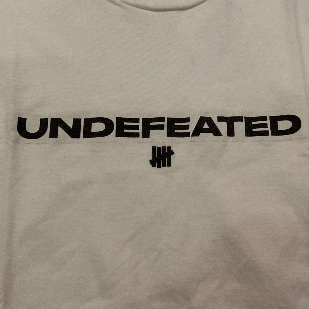 Undefeated White T-Shirt Size Small (Category: Tshirts & Polo Shirts ) located in Manila. Submitted by okeanos (Listing ID 1441773955, Image 2). Description: - Authentic Undefeated White T-Shirt - Size: Small - Features the iconic Undefeated logo prominently on the chest - Subtle Undefeated logo detail on the sleeve - Proudly made in Mexico - Ideal for casual and everyday wear.