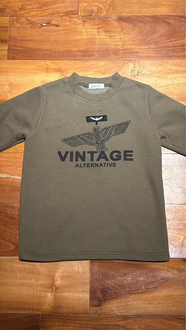 Vintage Alternative Eagle Graphic Crewneck Sweatshirt (Category: Babies & Kids Fashion) located in Pateros City. Submitted by eunikaesp92479 (Listing ID 1441752247, Image 2). Description: - Olive green crewneck sweatshirt - Features a black eagle graphic with 'VINTAGE ALTERNATIVE' text - Long sleeves with ribbed cuffs and hem - Classic and simple design - Ideal for casual wear.