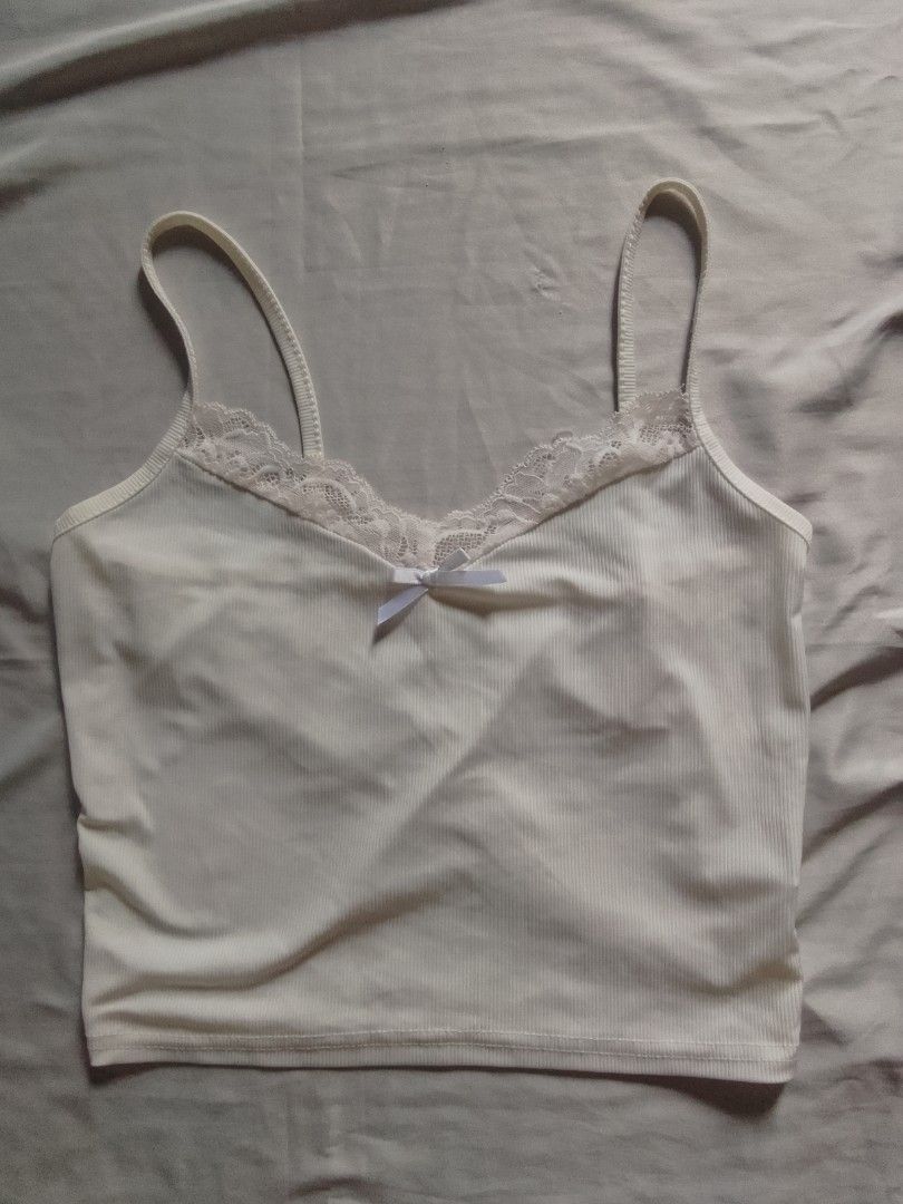 White Lace Trim Cami Top with Bow (Category: Sleeveless) located in Manila. Submitted by blessyfindsfashionclo (Listing ID 1441779973, Image 1). Description: - Ribbed white cami top - Delicate lace trim along the neckline - Small white bow detail at the center - Adjustable spaghetti straps - Versatile for layering or wearing solo.