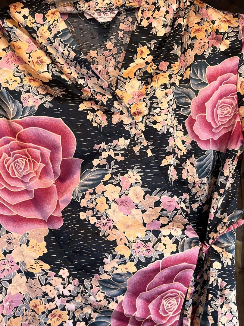 Floral Wrap Blouse with Tie Detail (Category: Blouses) located in Iloilo. Submitted by wanderzee (Listing ID 1446730812, Image 2). Description: - Elegant black blouse with a striking floral print. - Features prominent pink roses and delicate yellow and pink flowers. - Long sleeves for a sophisticated look. - Flattering wrap style with an adjustable side tie. - Fabric boasts a subtle, luxurious sheen. - Versatile piece: dress it up for events or d