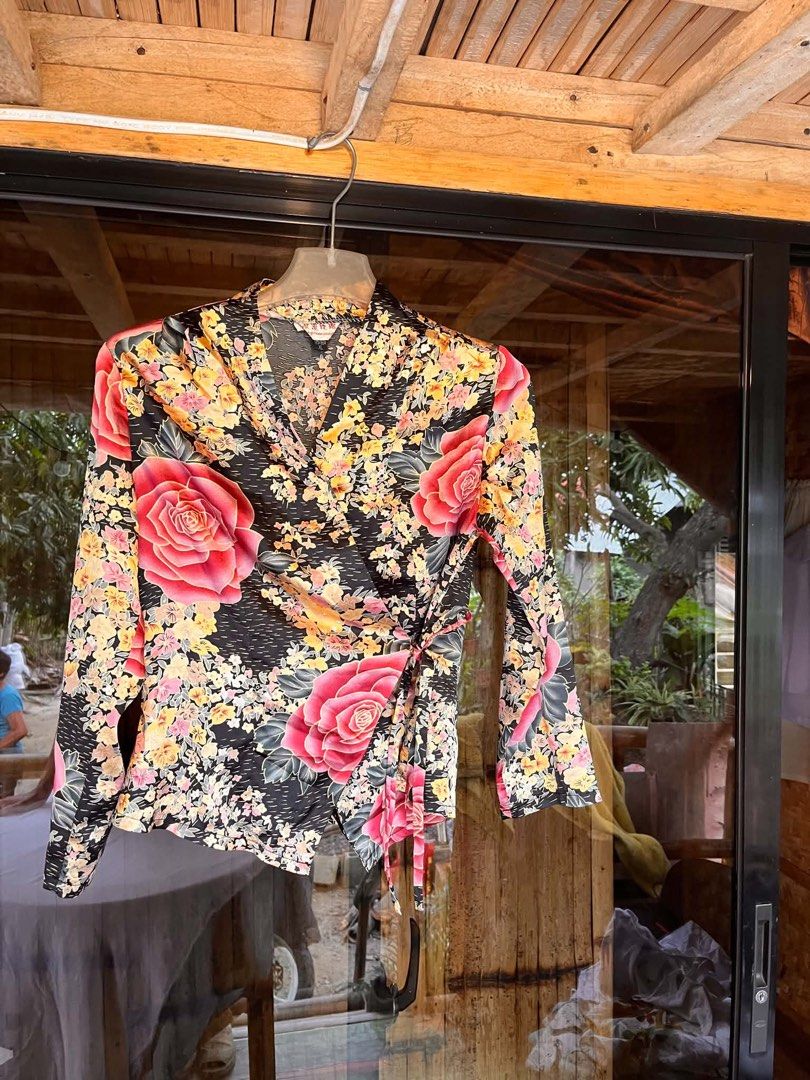 Floral Wrap Blouse with Tie Detail (Category: Blouses) located in Iloilo. Submitted by wanderzee (Listing ID 1446730812, Image 1). Description: - Elegant black blouse with a striking floral print. - Features prominent pink roses and delicate yellow and pink flowers. - Long sleeves for a sophisticated look. - Flattering wrap style with an adjustable side tie. - Fabric boasts a subtle, luxurious sheen. - Versatile piece: dress it up for events or d