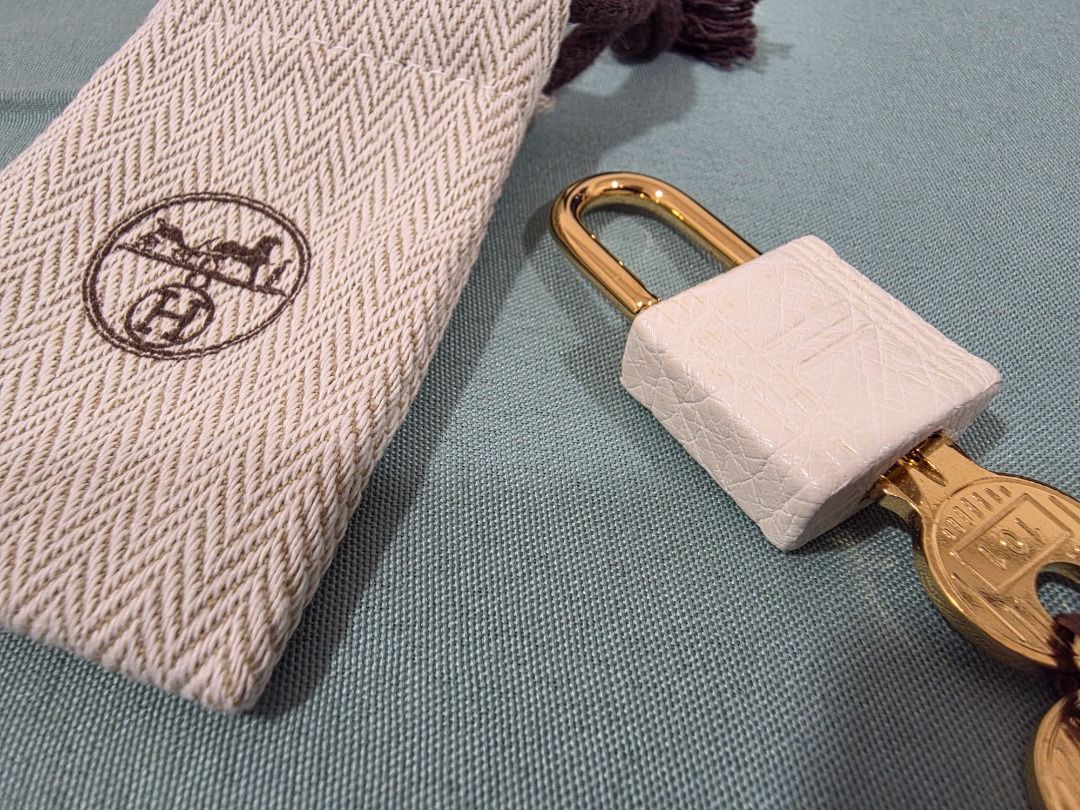 Hermes Lock and Key with Dust Bag2 (Category: Luxury Bags & Wallets) located in Cordon. Submitted by jrluxurs (Listing ID 1446896599, Image 3). Description: - Authentic Hermes lock and key set - Includes original dust bag - Gold hardware - Lock features a white textured leather casing - Key is engraved with '101' - Ideal for accessorizing bags or as a collectible item.
