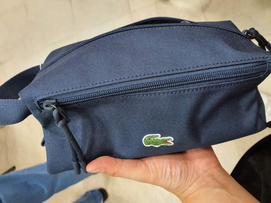 Lacoste Navy Blue Pouch Bag (Category: Luxury Bags & Wallets) located in Manila. Submitted by dominic000 (Listing ID 1446758276, Image 1). Description: Navy blue pouch from Lacoste. Has a main zippered compartment and a front zippered pocket. The material looks durable and water-resistant. Has a small handle on the side. Great for toiletries or small essentials. Measures about 9 inches long. PROMO!!!! brand new, original, not fake. never been use