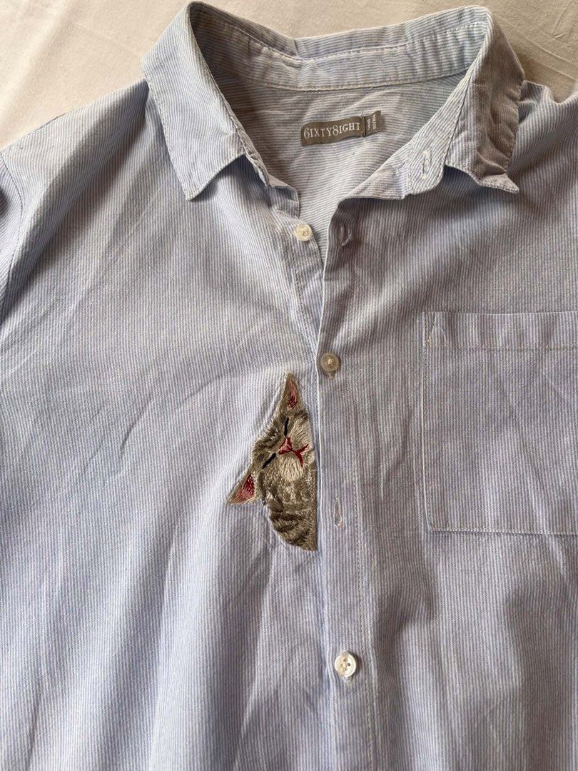 Sixty8ight Striped Button-Up Shirt with Cat Embroidery (Category: Shirts) located in Iloilo. Submitted by wanderzee (Listing ID 1446731091, Image 2). Description: - Light blue and white striped button-up shirt - Adorable embroidered cat detail peeking from pocket - Long sleeves, can be cuffed for versatile styling - Ideal for casual everyday wear - Tagged size 11 -lakas maka rich-tita vibe Bust 40” Shoulder 16” Length 32” .