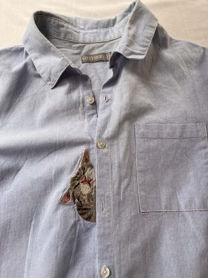 Sixty8ight Striped Button-Up Shirt with Cat Embroidery (Category: Shirts) located in Iloilo. Submitted by wanderzee (Listing ID 1446731091, Image 3). Description: - Light blue and white striped button-up shirt - Adorable embroidered cat detail peeking from pocket - Long sleeves, can be cuffed for versatile styling - Ideal for casual everyday wear - Tagged size 11 -lakas maka rich-tita vibe Bust 40” Shoulder 16” Length 32” .