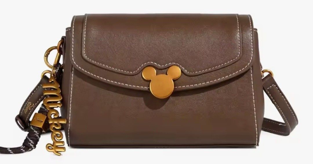 Brown Disney Mickey Mouse Crossbody Bag (Category: Cross-body Bags) located in Quezon City. Submitted by mimil_ (Listing ID 1441790493, Image 3). Description: - Cute brown crossbody bag - Features a Mickey Mouse clasp and "Mickey" charm - Comes with a stylish patterned strap - Perfect for everyday use or a fun Disney trip - Small and compact, ideal for carrying essentials - Detailed stitching on the flap -Bought at Laz*da Mall Disney Fashion Stor
