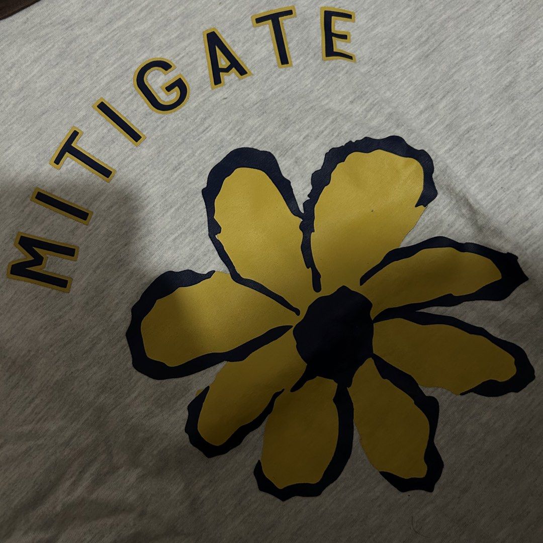 MNL Grey T-shirt with Flower Graphic and "MITIGATE" Text (Category: Tshirts & Polo Shirts ) located in Antipolo. Submitted by wrdrb.co (Listing ID 1441909821, Image 3). Description: - Brand: MNL - Color: Grey - Graphic: Yellow flower with dark blue outline - Text: "MITIGATE" above graphic - Details: Brown ribbed collar and sleeve cuffs - Style: Casual, comfortable - Occasion: Everyday wear.